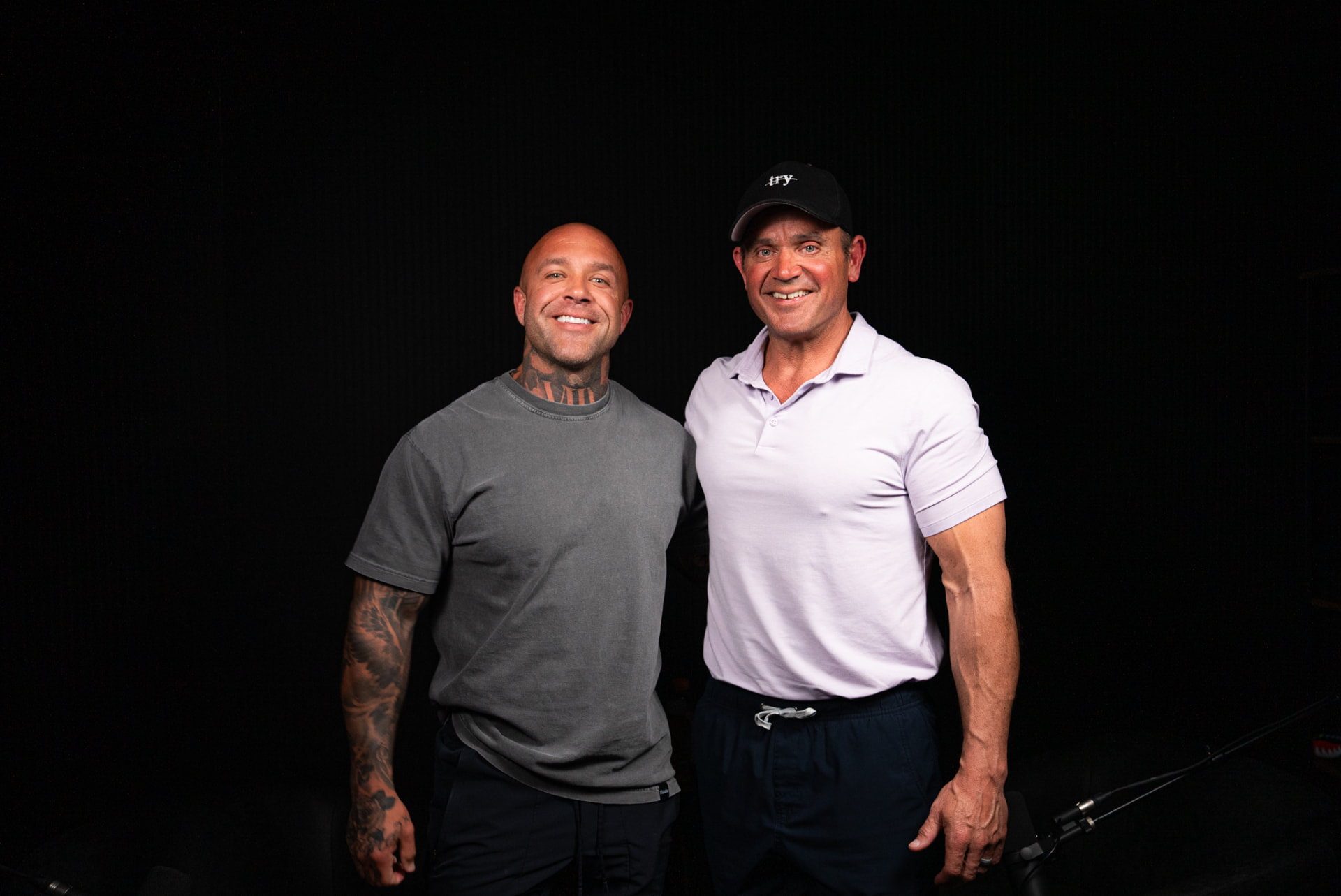 Two men posing together on a dark podcast set