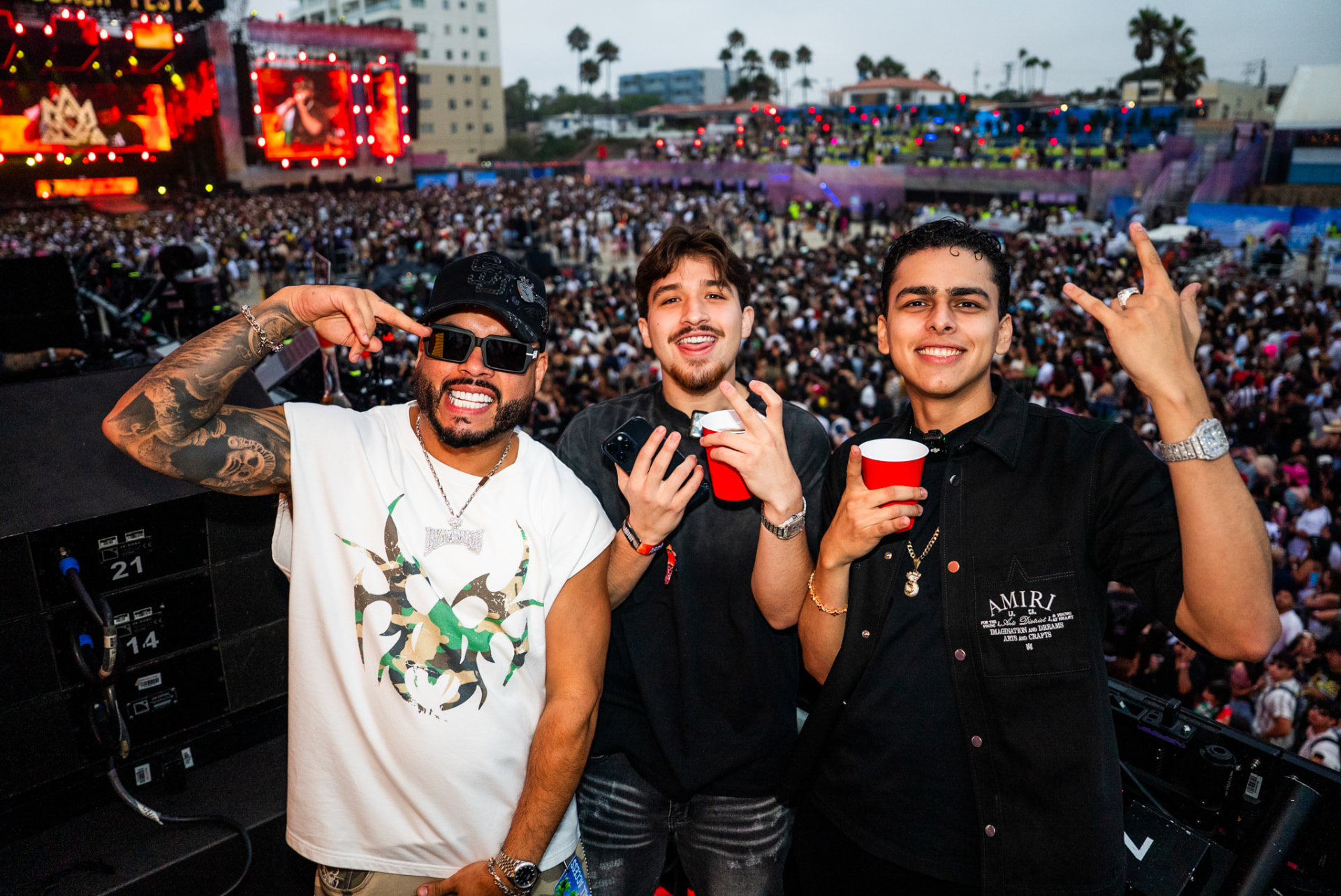 Three friends posing above a large outdoor festival crowd