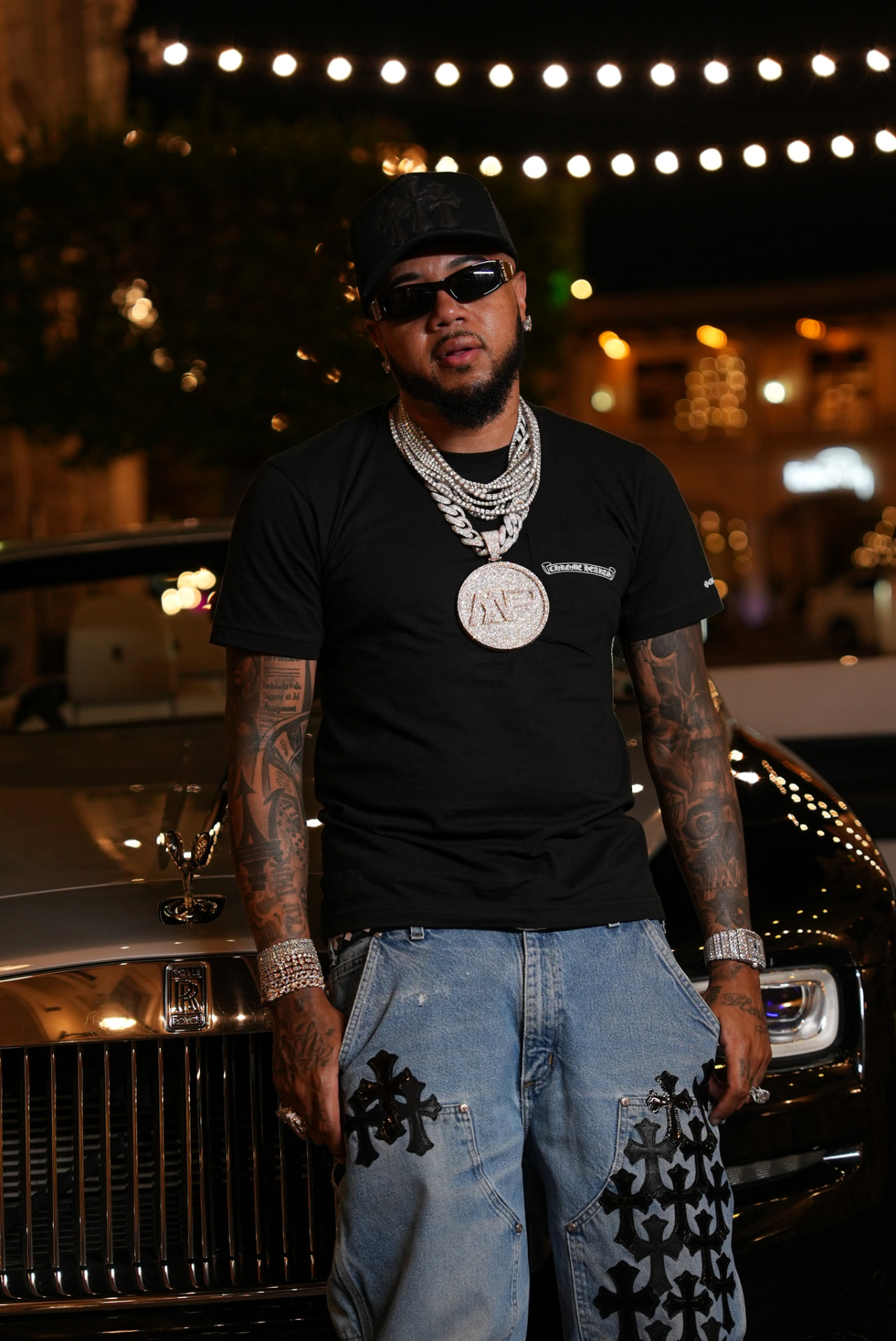 Artist layered in chains standing in front of a Rolls-Royce at night