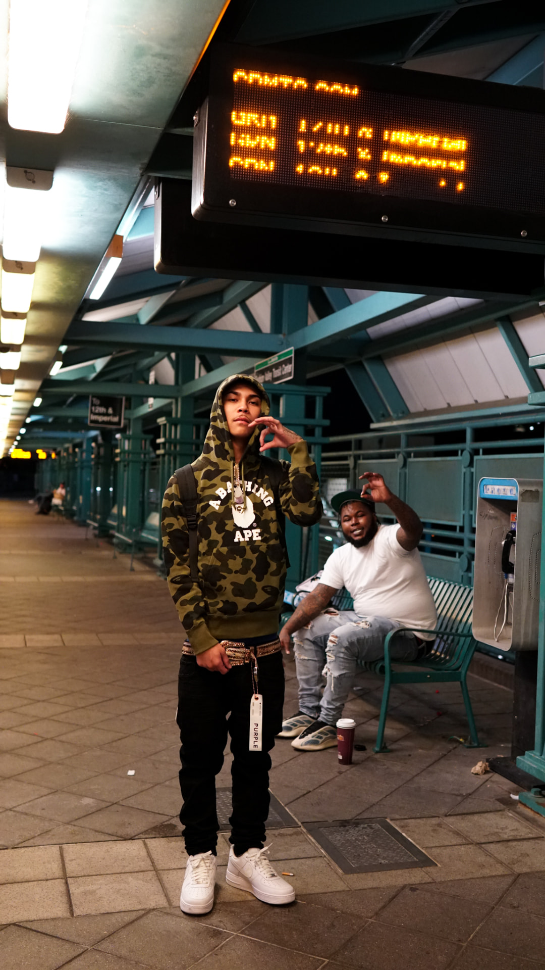 Two artists posing on a lit transit platform at night