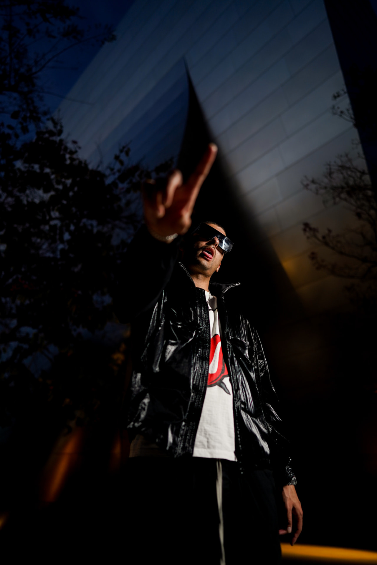 Low-angle portrait of an artist in a black leather jacket against a mirrored building