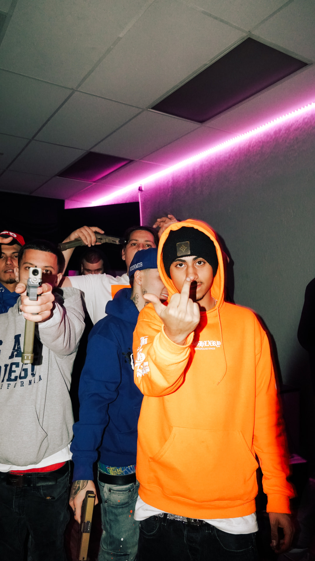 Group of artists posing in a pink-lit room, one in an orange hoodie
