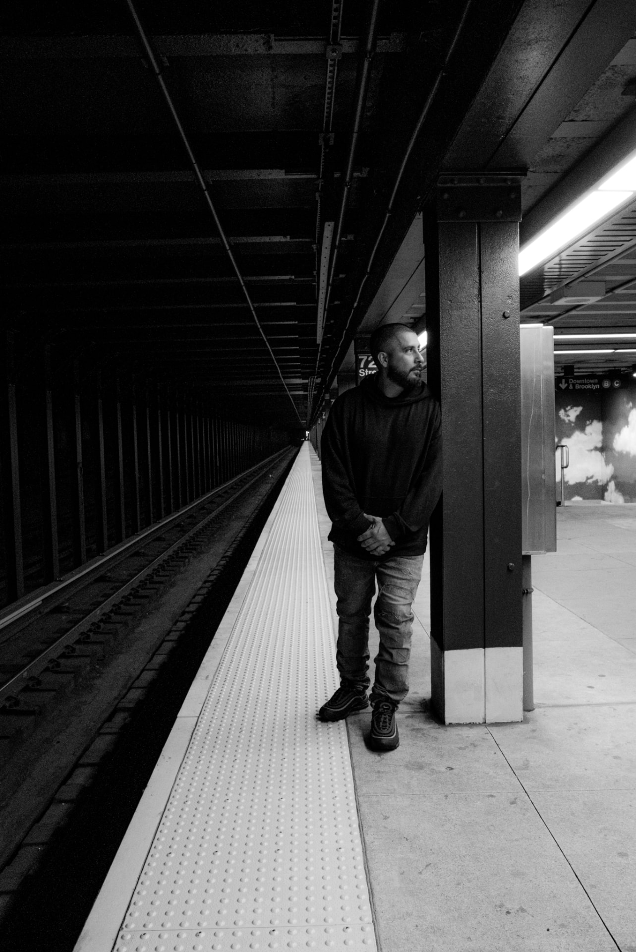 Black-and-white portrait of a man waiting beside a subway track