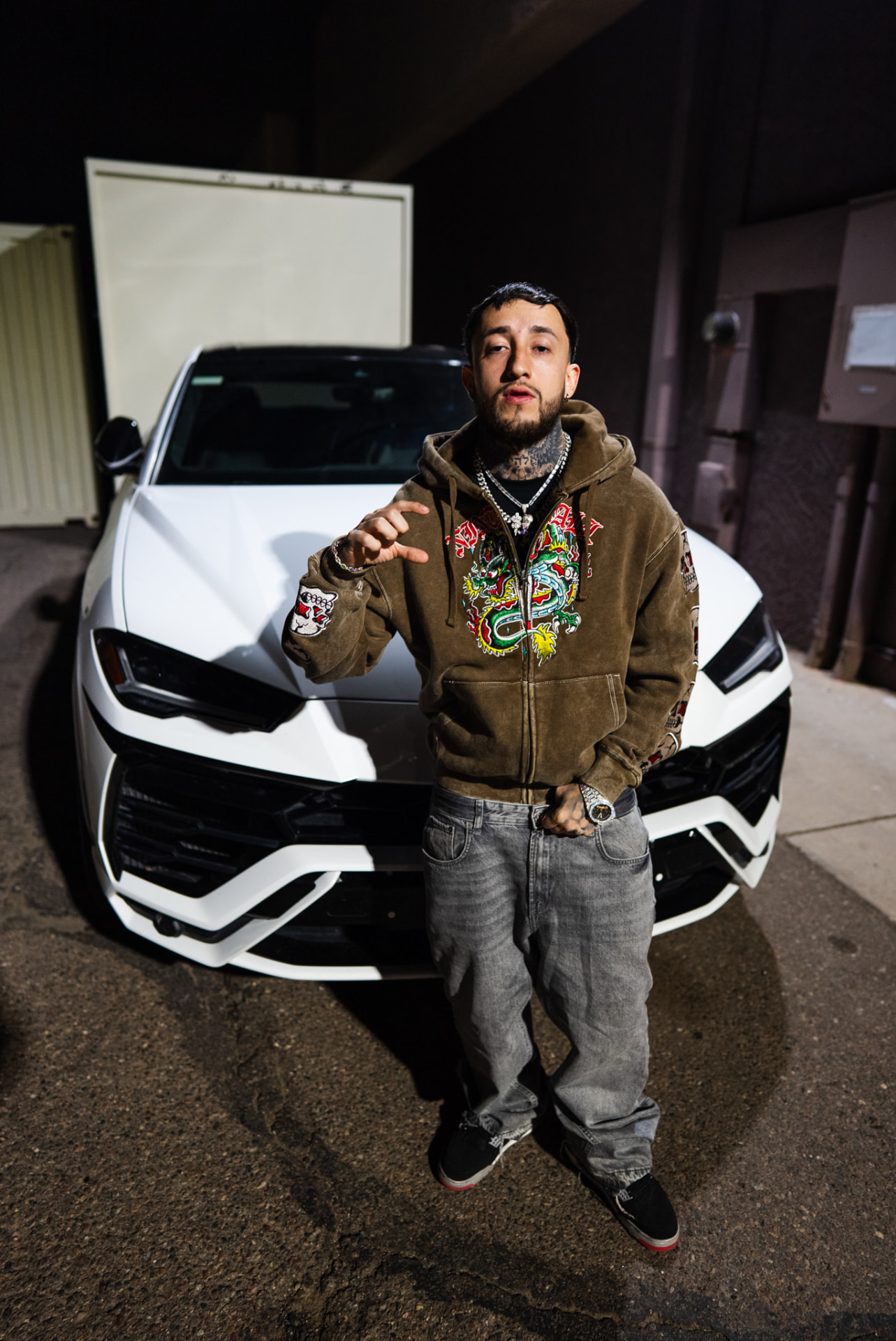 Artist posing in front of a white performance SUV at night