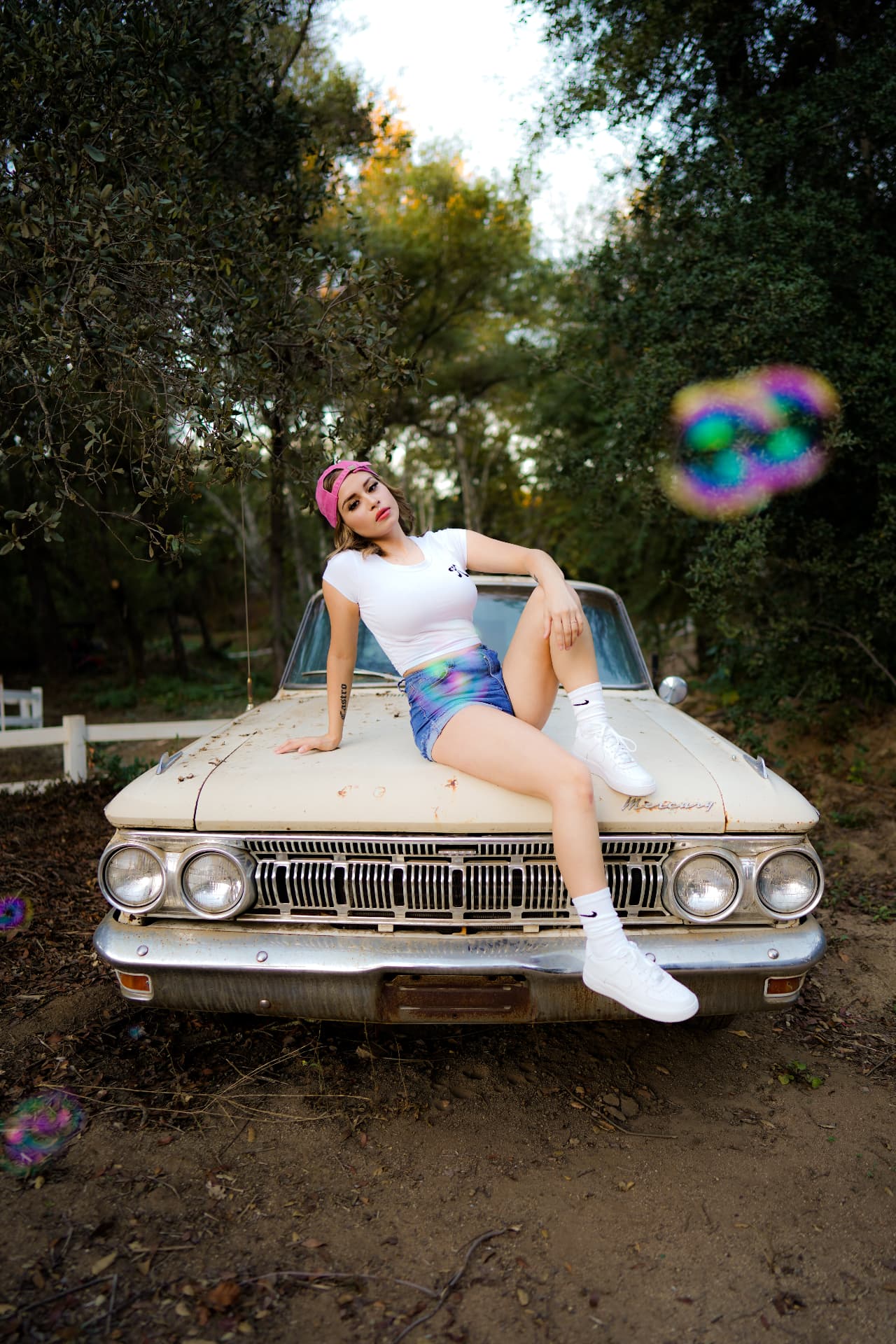 Woman in a white tee and denim shorts posed on a vintage car hood
