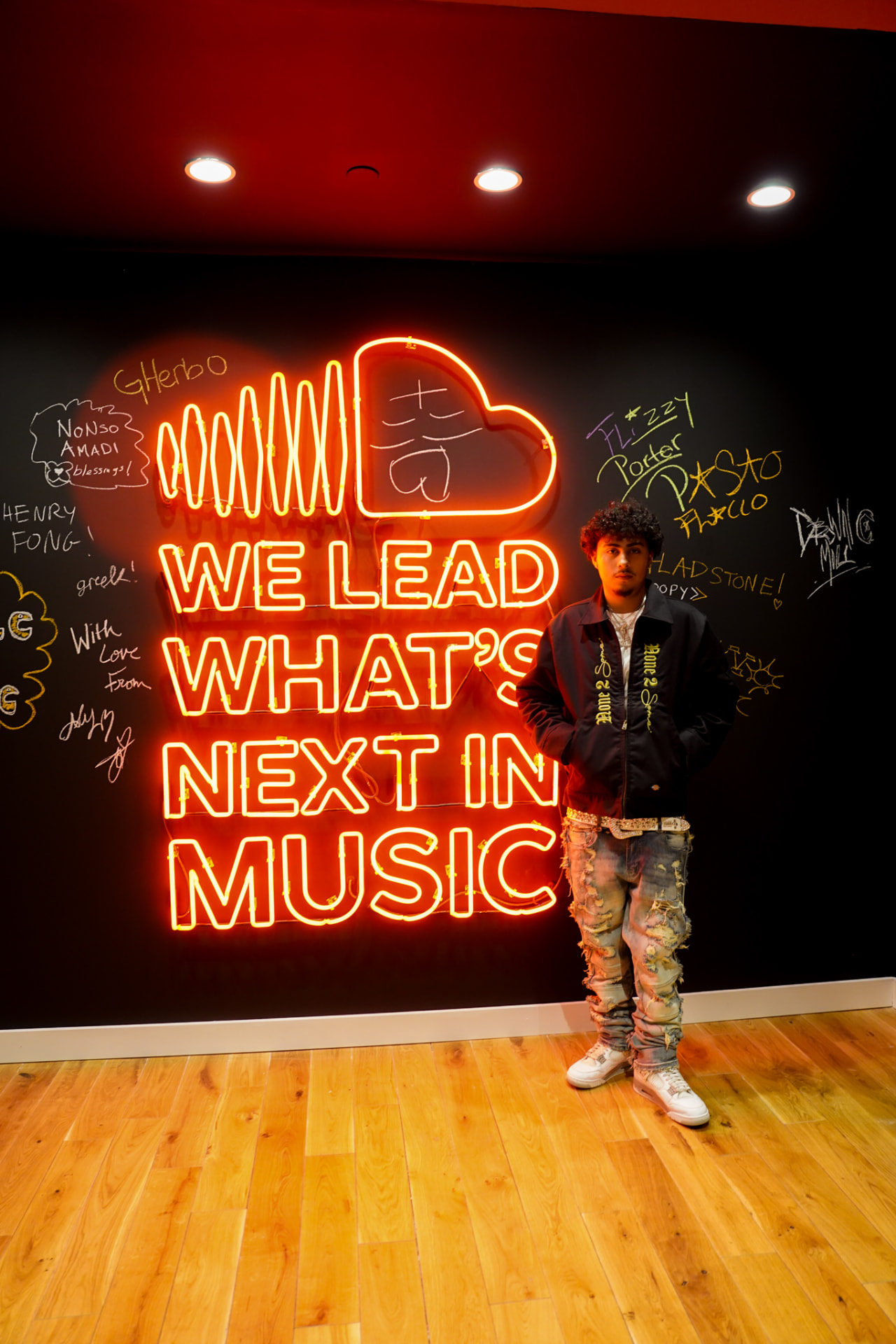 Artist standing in front of a neon SoundCloud sign on a signed wall