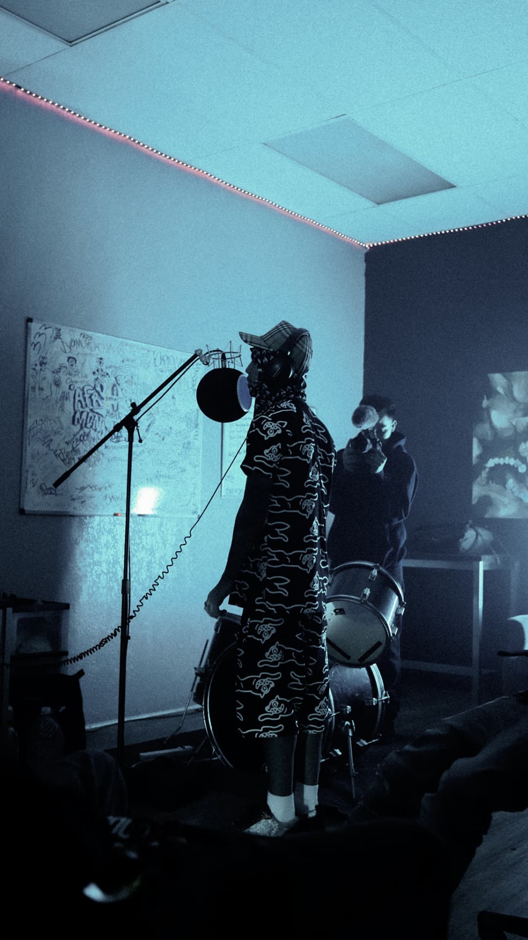 Artist recording in a teal-lit studio room beside a drum kit