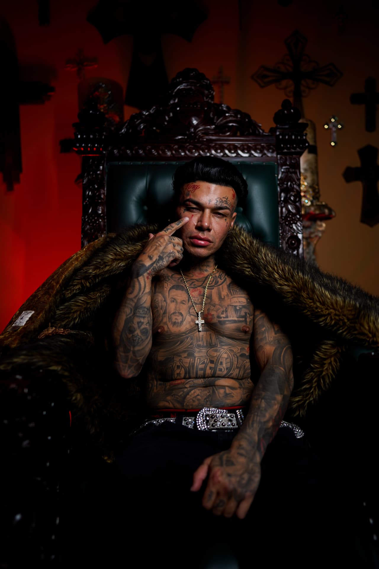 Tattooed artist seated in an ornate chair under red light