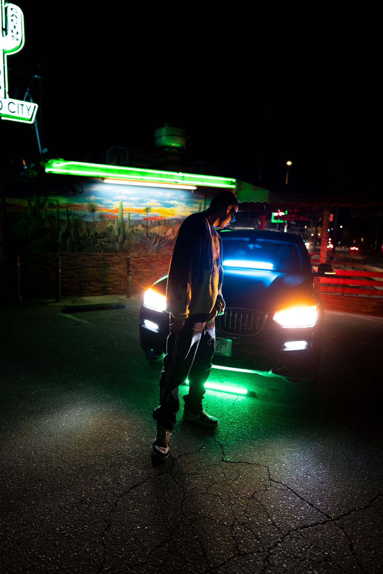Artist standing in front of an underglow-lit SUV beside a neon diner