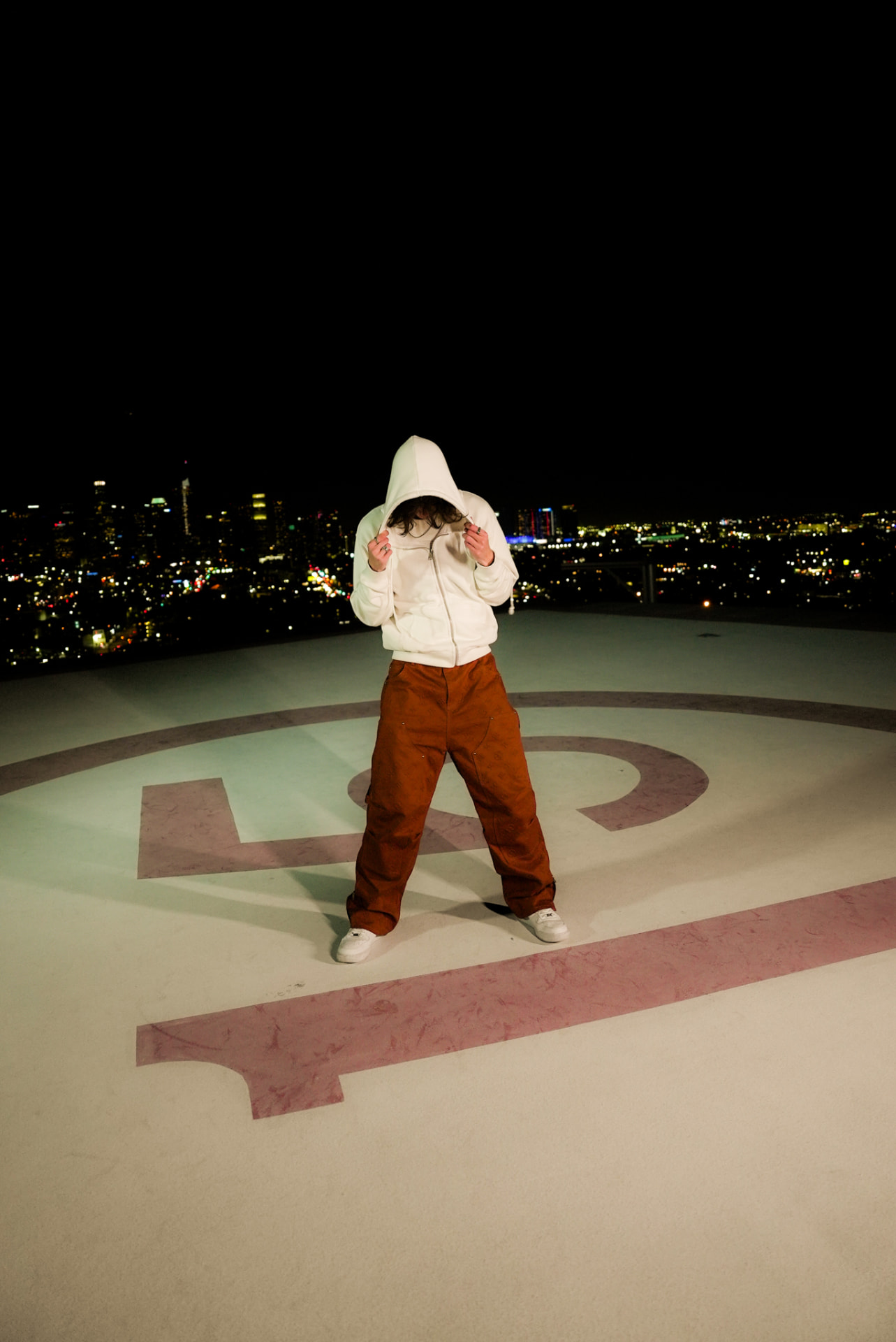 Artist in a white hoodie standing on a helipad at night