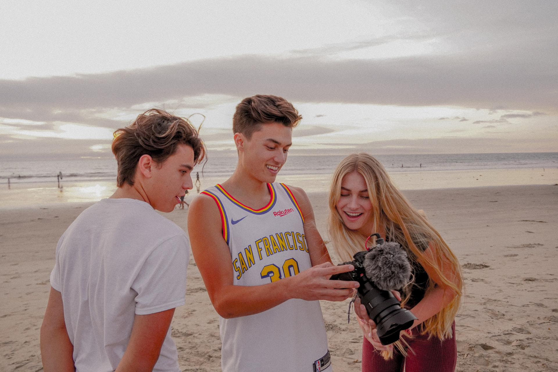 Three people reviewing camera footage on a beach at sunset