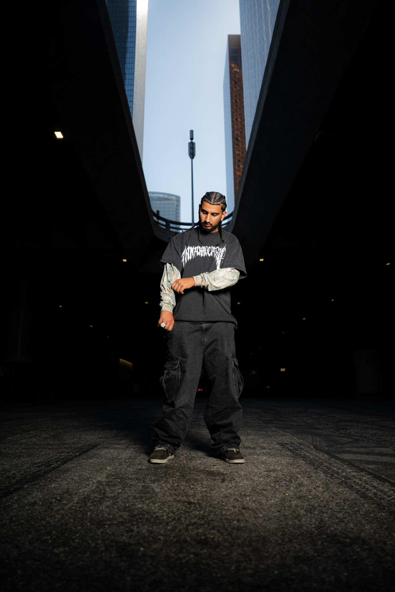 Artist standing between downtown high-rises in baggy black denim
