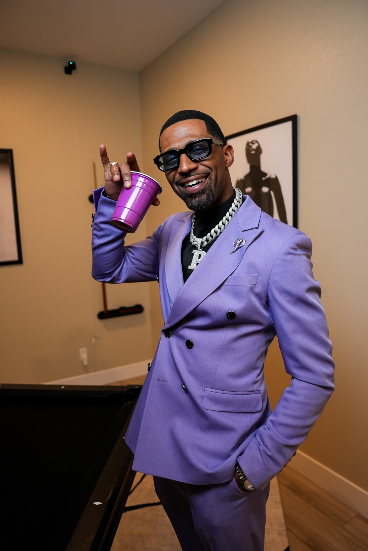 Artist in a lavender suit raising a purple cup indoors