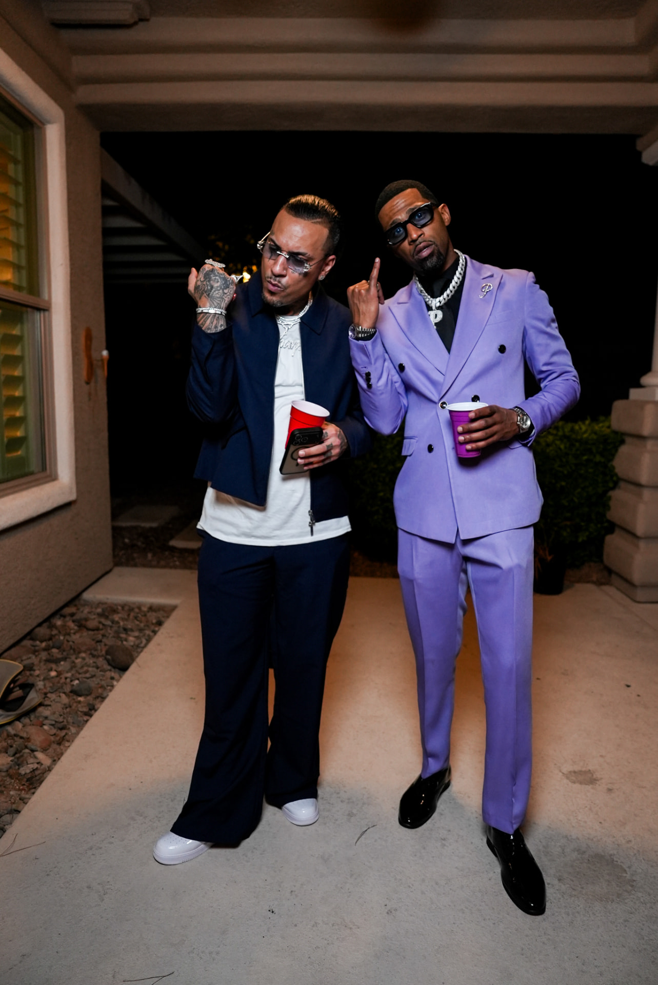 Two artists in tailored suits posing with cups outside at night