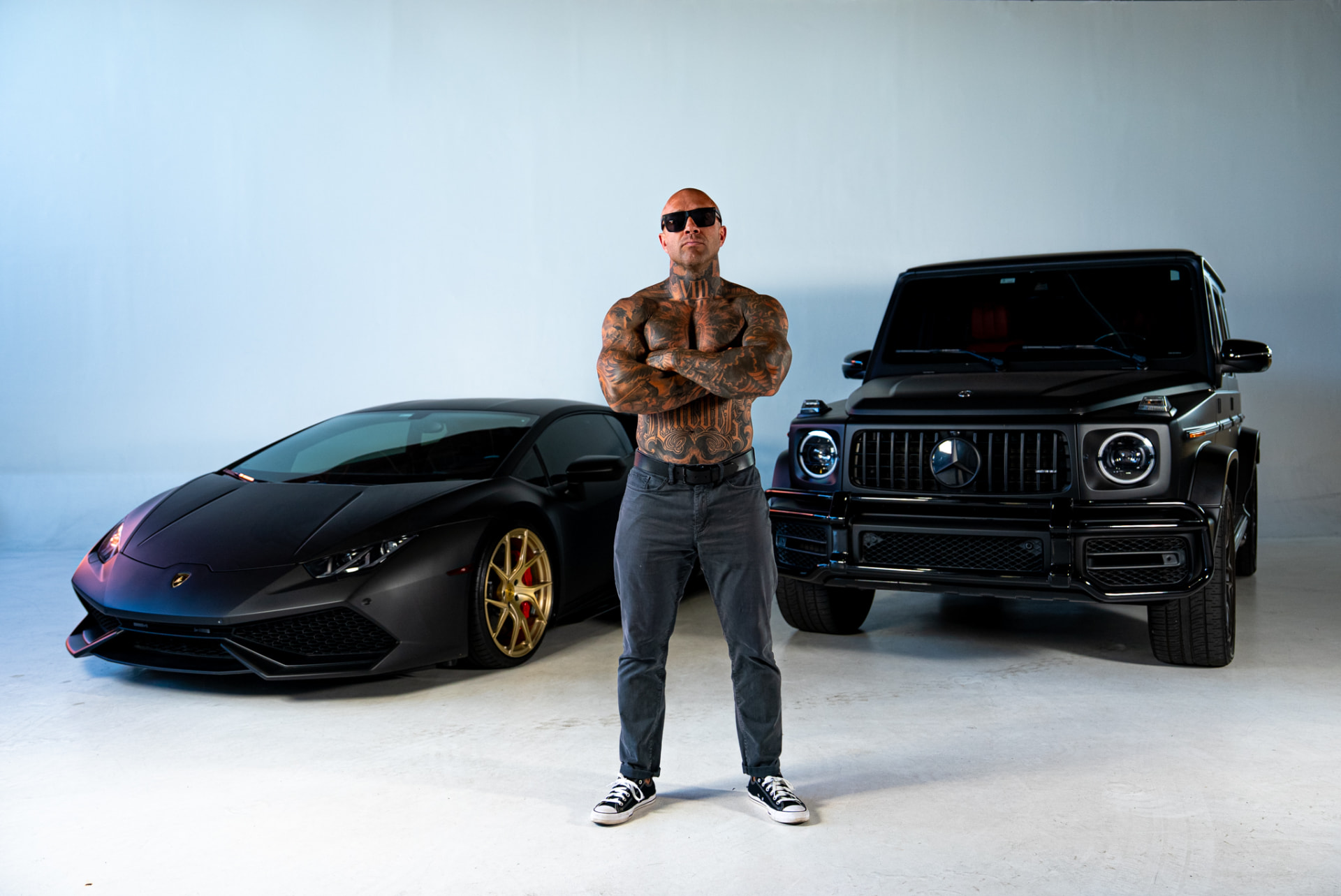 Tattooed athlete standing between a Lamborghini and Mercedes SUV