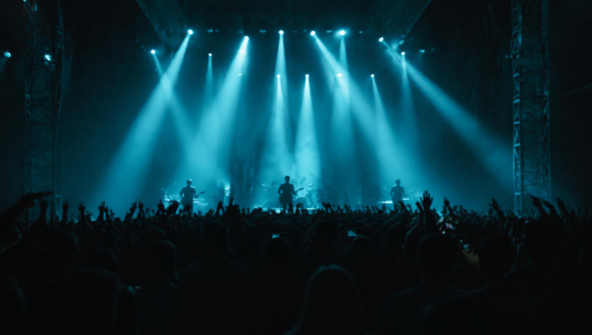 Concert stage lit by cool cyan light beams above a silhouetted crowd